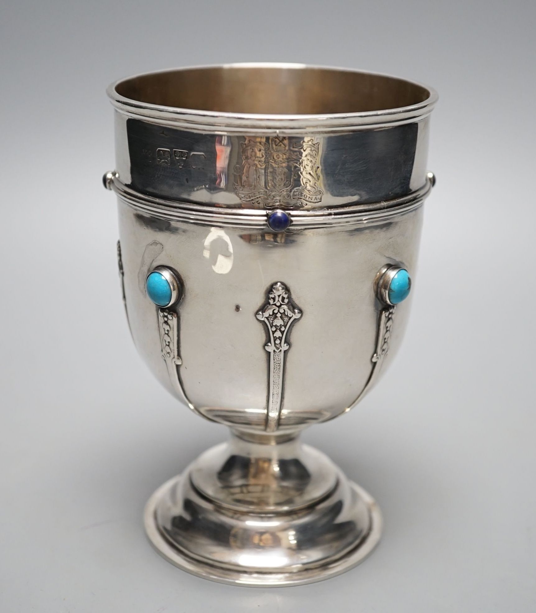 A George V silver goblet or pedestal cup with inset cabochon turquoise and cabochon lapis lazuli, with engraved crest and strapwork decoration, Henry Moreton, Chester, 1913, 13.6cm, gross weight 7oz.